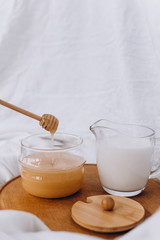 Honey and milk on a wooden stand. Honey drips on a stick. White fabric background