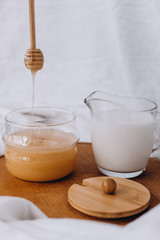 Honey and milk on a wooden stand. Honey drips on a stick. White fabric background