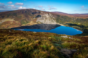 Naklejka na ściany i meble A blue lake below a mountain with reflection and a grassy landscape.