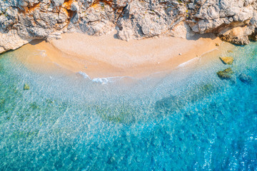 Aerial view of sandy beach with rocks and sea with transparent blue water at sunset. Coast of adriatic sea at sunset in summer. Top view. Landscape with clear azure water, waves, stones. Nature - obrazy, fototapety, plakaty