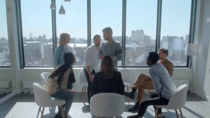 Mixed race team of anonymous gamers stand up and hugs new sad club member during a meeting in sunny office. Concept of bringing people together who share their experiences and hopes with each other