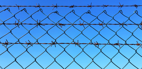 Barbed wire on blue sky background. Prison and freedom. Panorama.