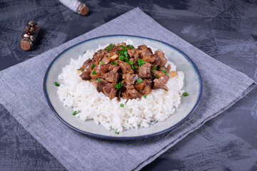 Stewed chicken gizzards on the boiled rice. Hot meal with offal meat products