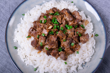Stewed chicken gizzards on the boiled rice. Hot meal with offal meat products