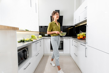 Woman cooking healthy food on the modern kitchen at home, wide interior view. Woman is motion blurred