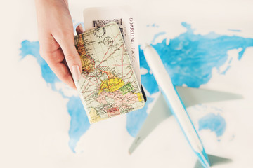 Passport and boarding pass in woman's hands on background of world map and airplane