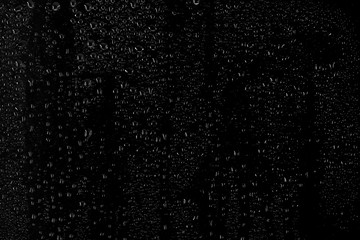 Drops of water flow down the surface of the clear glass on a black background.	