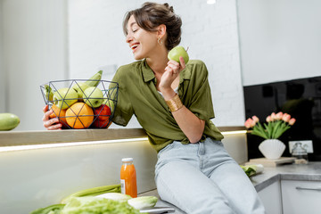 Portrait of a young and cheerful woman with healthy raw food on the kitchen at home. Vegetarianism,...