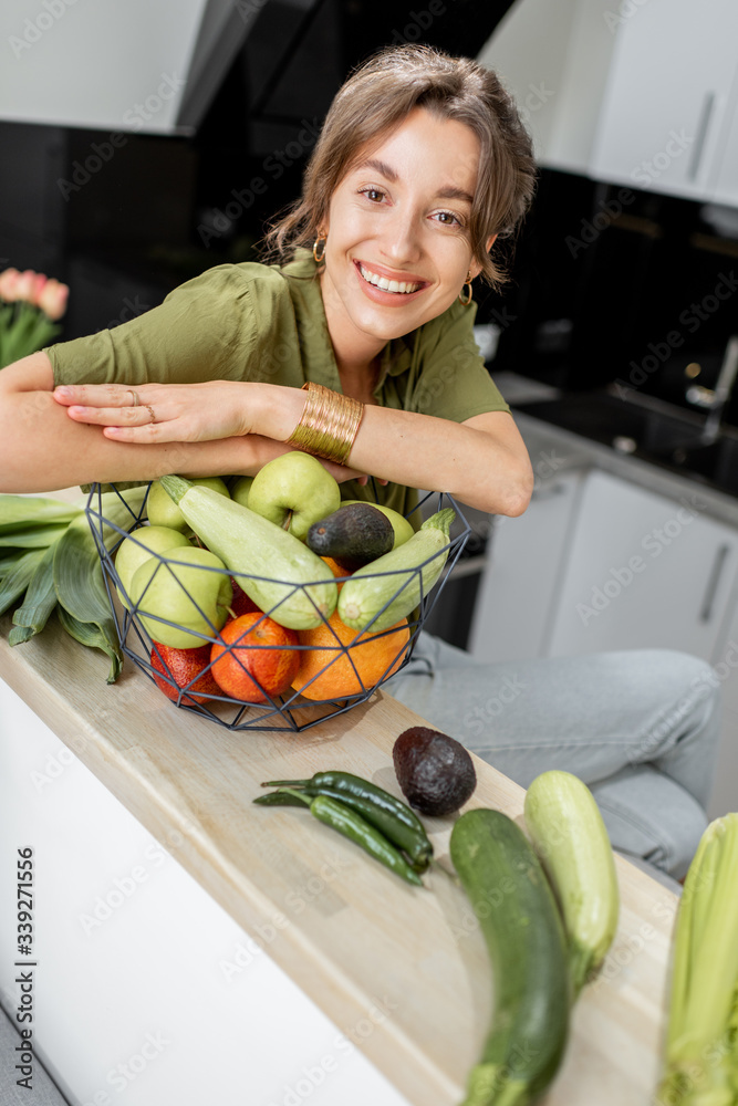 Wall mural portrait of a young and cheerful woman with healthy raw food on the kitchen at home. vegetarianism, 