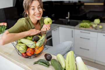 Portrait of a young and cheerful woman with healthy raw food on the kitchen at home. Vegetarianism,...