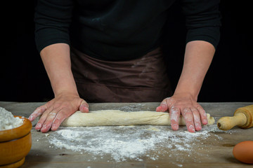 Man hands kneading bread dough on a wooden table with black background