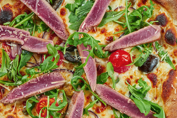 Appetizing baked pizza with tuna, arugula, cherry tomatoes and parmesan with crisp on a wooden background. Restaurant serving. Seafood pizza. Top view, close up on texture