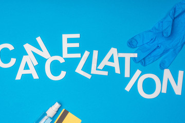 Top view of lettering cancellation with bottle of hand sanitizer, latex glove and credit card on blue background