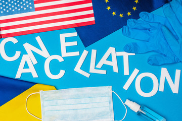 Top view of flags of Ukraine, european unity and america near lettering cancellation and medical mask on blue background