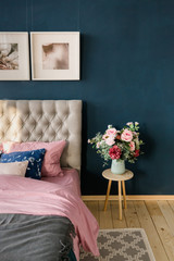 a blue vase with flowers between a grey English chair and a bed with a headboard in a carriage tie in a luxurious blue interior with paintings
