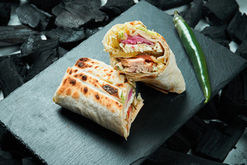 Appetizing shaurma or shawerma with spices and onions on a black slate tray on a background of charcoal. Kebab