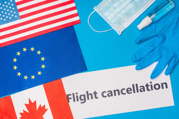 Top view of card with flight cancellation lettering near medical mask and flags of countries on blue surface