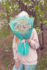 Stylish young woman florist holds in her hands a large bouquet of colored gypsophila packed in tiffany color paper. The concept of floristry and holiday
