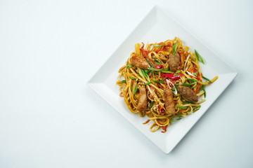Tasty udon noodles in sweet and sour sauce with vegetables and pork meat plate on a gray...