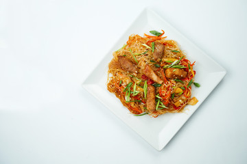 Tasty udon noodles in sweet and sour sauce with vegetables and pork meat plate on a gray background. Top view with copy space