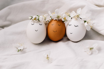 Funny easter eggs with wreaths of flowers. Easter composition on white fabric background