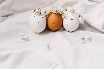 Funny easter eggs with wreaths of flowers. Easter composition on white fabric background