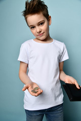 Small cute boy with modern hairstyle in stylish casual clothing standing and showing few coins from black purse in hand