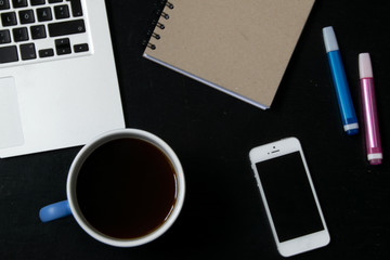 View from above of modern workplace with cup of tea, laptop keyboard, mobile phone, pens and notebook on black wooden table
