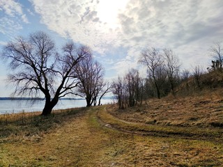 spring Sunny landscape by the river against the background of trees and blue sky with clouds