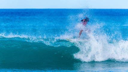 Vague sur laquelle un surfeur est pris dans les embruns dans une mer bleu d'azur avec un ciel bleu...