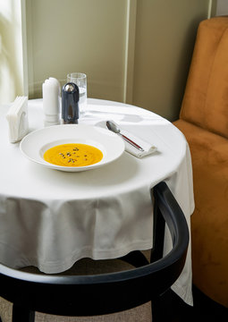Homemade creamy pumpkin soup topped with olive oil and toasted pumpkin seeds on white table