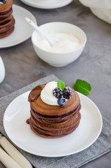 Stack of chocolate pancakes on a white plate with chocolate sauce, whipped cream, blueberries and blackberries on top of a concrete background. Delicious breakfast. Vertical orientation. Copy space.