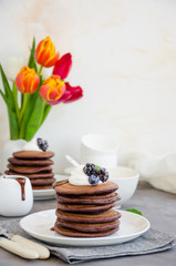 Stack of chocolate pancakes on a white plate with chocolate sauce, whipped cream, blueberries and blackberries on top of a concrete background. Delicious breakfast. Vertical orientation. Copy space.