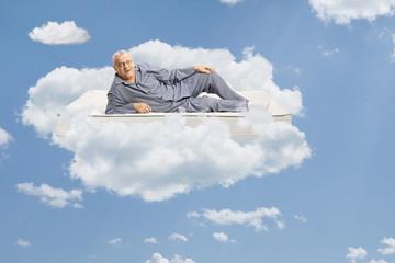 Mature man in pajamas lying on a bed mattress and floating in the sky