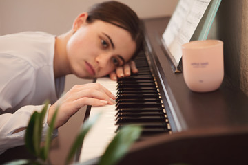Bored girl lies on piano keys. The concept of quality education, distance learning, home quarantine, personal isolation