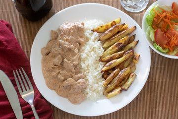 beef stroganoff with rice and french fries on white plate 