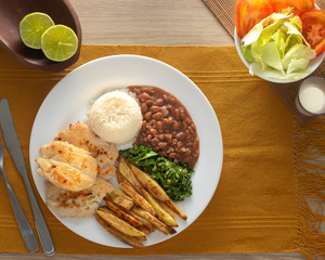 Dish of grilled chicken fillet with rice, beans, french fries, kale and salad on white plate. Top view.