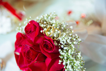 Red ribbon . Red engagement flowers on white table . Bride and groom with Engagement gold rings put on the red wedding bouquet . Red engagement bouquet .