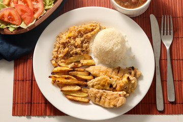Dish of grilled chicken fillet with rice, beans, french fries and farofa on white plate. Top view.
