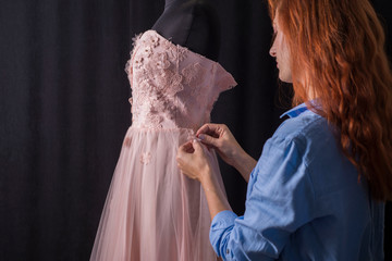 the process of making clothes. Professional designer, handmade craftsman, sews flowers on a pink dress, on a mannequin, in the studio