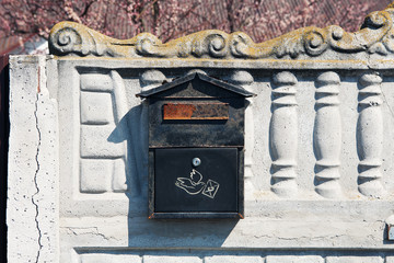 Old mail box for letters with metal box with rust hanging on fence on background of flowering trees