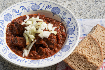 Close up Picture of Czech style beef goulash served in rustic deep plate with chopped onion on the top and slice of traditional bread. Made from slow cooked beef with sweet pepper. Traditional dish.