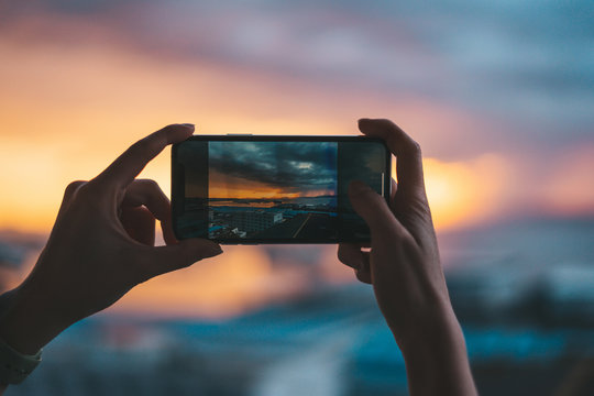 Hands holding a smartphone taking a photograph of the sea at sunset