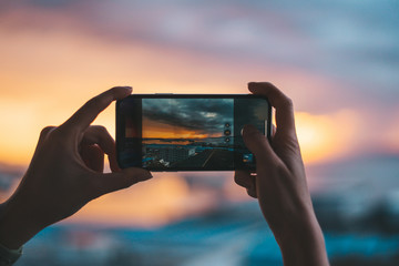 Hands holding a smartphone taking a photograph of the sea at sunset
