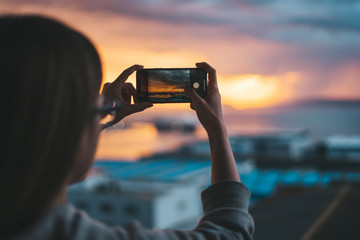Woman taking photos of the sea from the balcony with a smartphone - obrazy, fototapety, plakaty