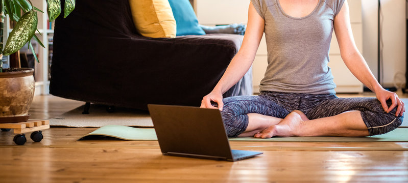 woman doing yoga workout at home watching videos online on laptop computer