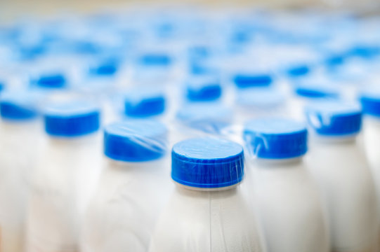 white plastic bottles with blue caps sealed in film. goods from the factory for sale in supermarkets. packaging of dairy products
