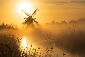 Yellow sunrise with traditional, Dutch windmill and a canal in the spring fog.
