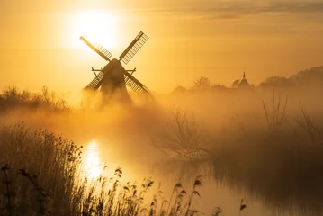Selbstklebende Fototapeten Melone Yellow sunrise with traditional, Dutch windmill and a canal in the spring fog.  © sanderstock
