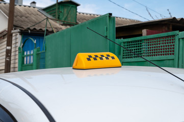 black-yellow checker taxi on a white car on a background of a green fence. permission to transport passengers. make money on delivery